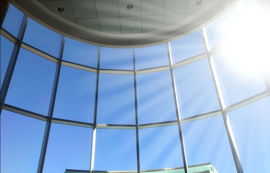 Sunlight streaming through a curved wall of tall glass windows into a building atrium