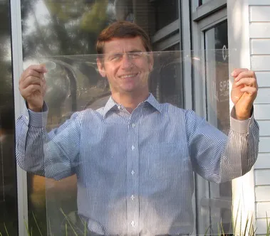 A man holding up a transparent sample sheet of the daylighting window film in front of a house