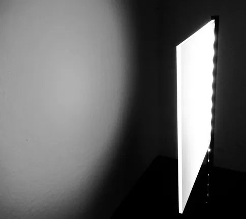 Edge-lit light guide panel in a dark room casting a directional beam of light onto a wall