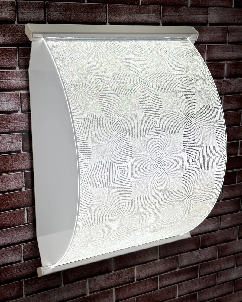 Curved CoreGLO wall sconce with a geometric pattern of concentric diamonds, lit, on a brick wall