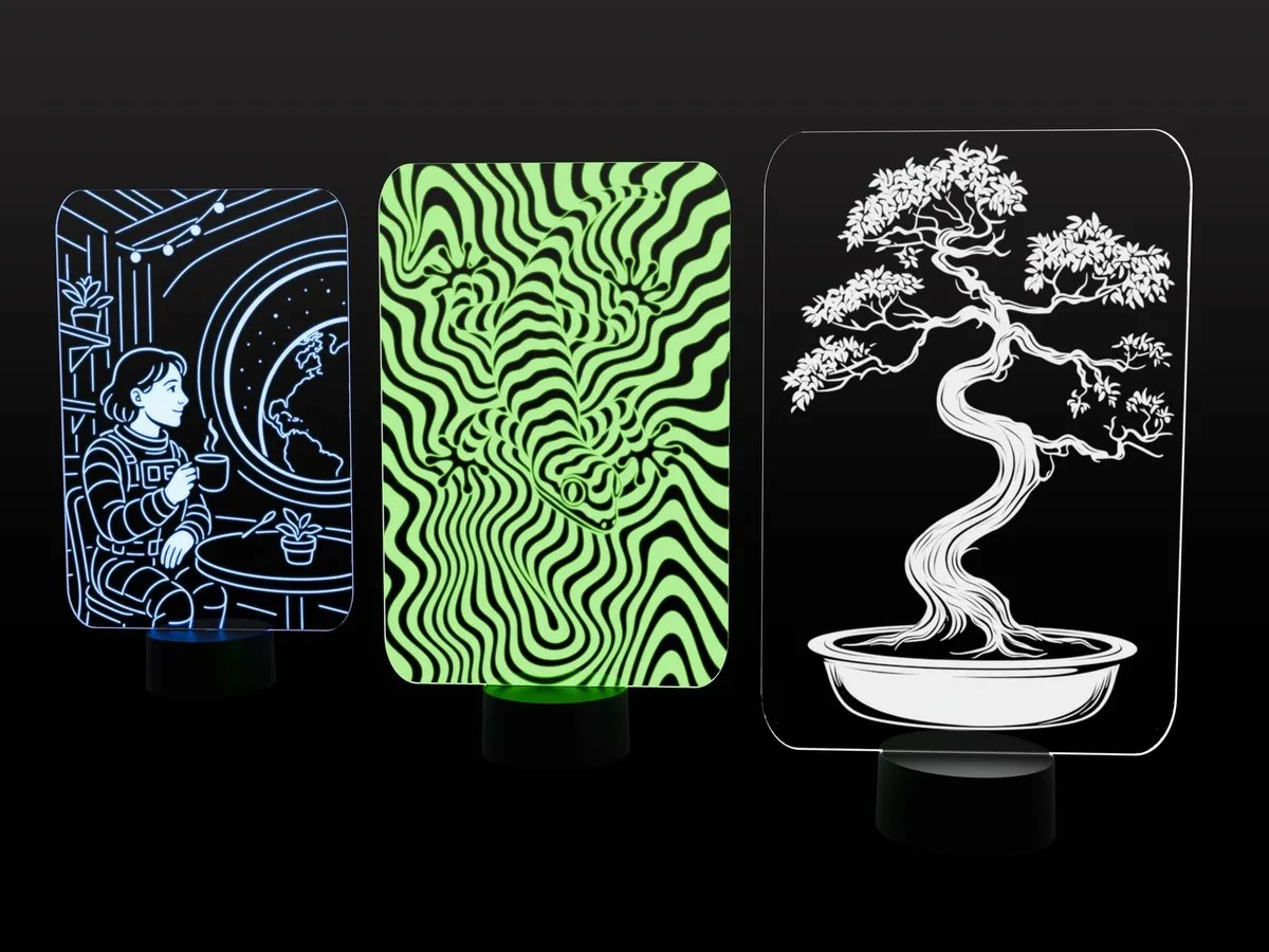 Three lit acrylic night lights on black bases: an astronaut in a space café, a green wavy gecko pattern and a bonsai tree