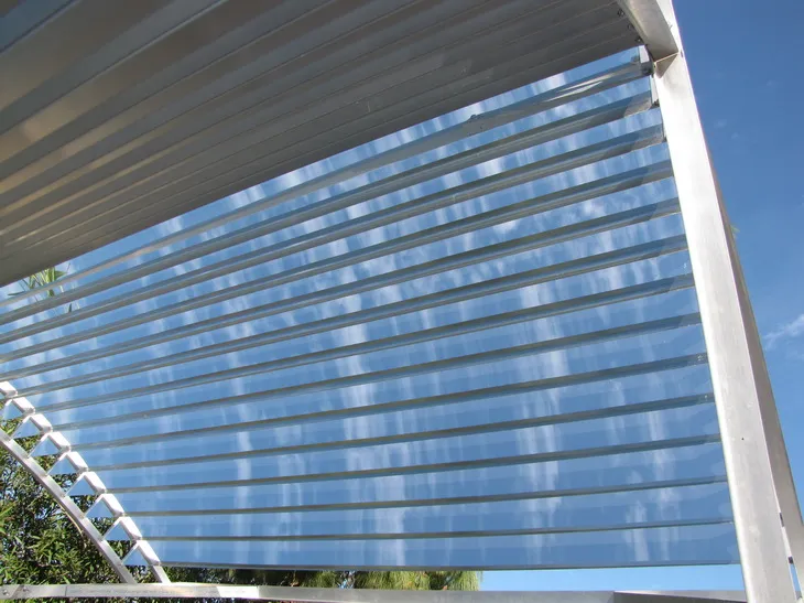 Slat-array concentrator with parallel mirror slats on a metal frame against a blue sky