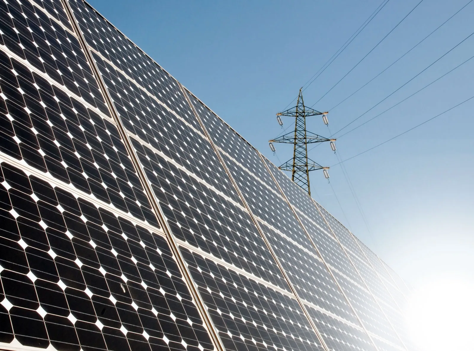 Rows of solar panels with a high-voltage transmission tower against a blue sky